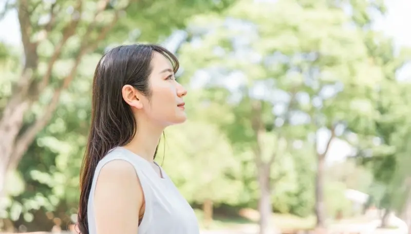 緑の中で空を見上げる若い女性の横顔