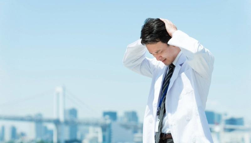 青空の下で頭を抱える白衣を着た男性