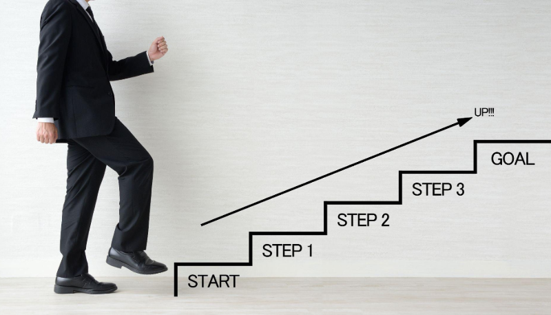 男性がステップアップの階段を上ろうとしている図